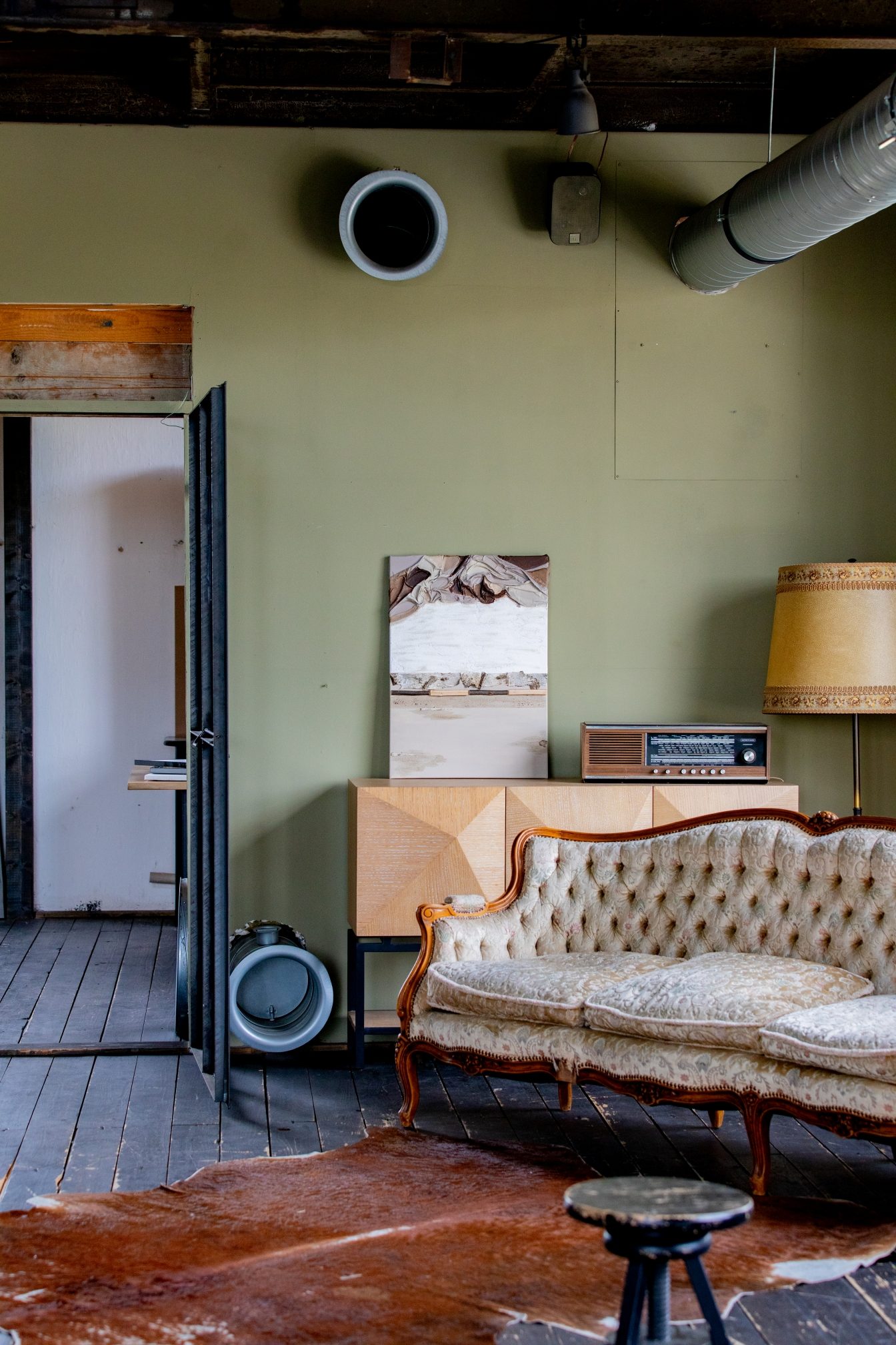 Artearth-Werke an einer waldgrünen Wand mit Vintage-Sofa